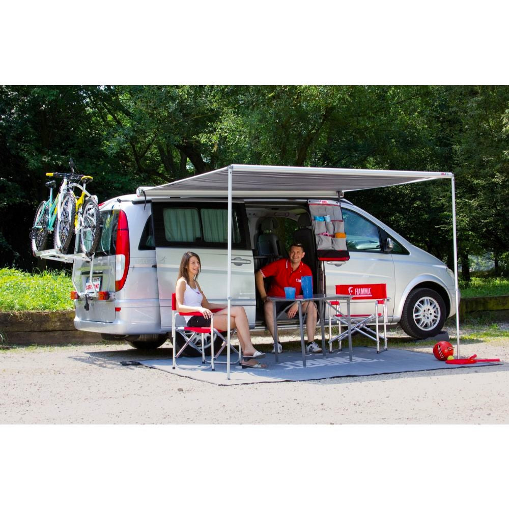 fiamma f35 pro lifestyle image that shows two people sitting around a table underneath their fully extended RV awning that is attached to a silver van side view