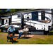airskirts reviews inflatable rv skirting kit trailer on grass midday with tubes placed underneath and two people sitting in chairs in front 