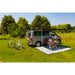 fiamma f35 300 lifestyle image that shows a family sitting under their fully extended RV awning sitting at a table reading a book
