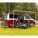 fiamma f35 pro 180 lifestyle image that shows two people sitting in chairs under their fully extended RV awning attached to a white and red van